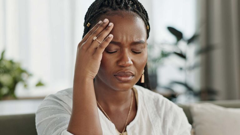 Woman with headache sitting on sofa.