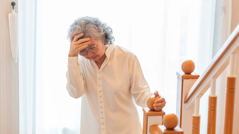 Senior woman looking stressed while holding her head on a staircase.